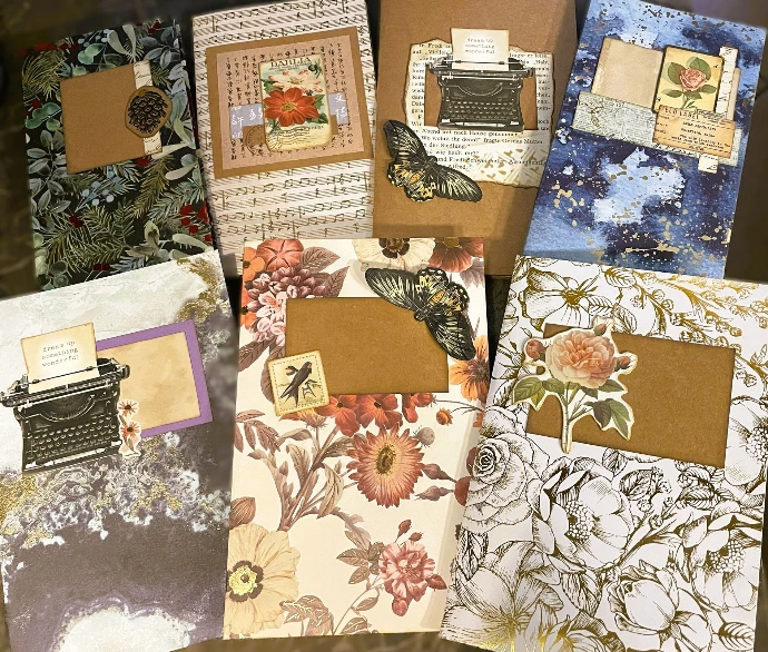 Journals faits à la main en papiers de design dans des couleurs douces et naturelles avec des éléments vintage typiques, comme une machine à écrire, une rose, des billets ; parfois ornés d'or.